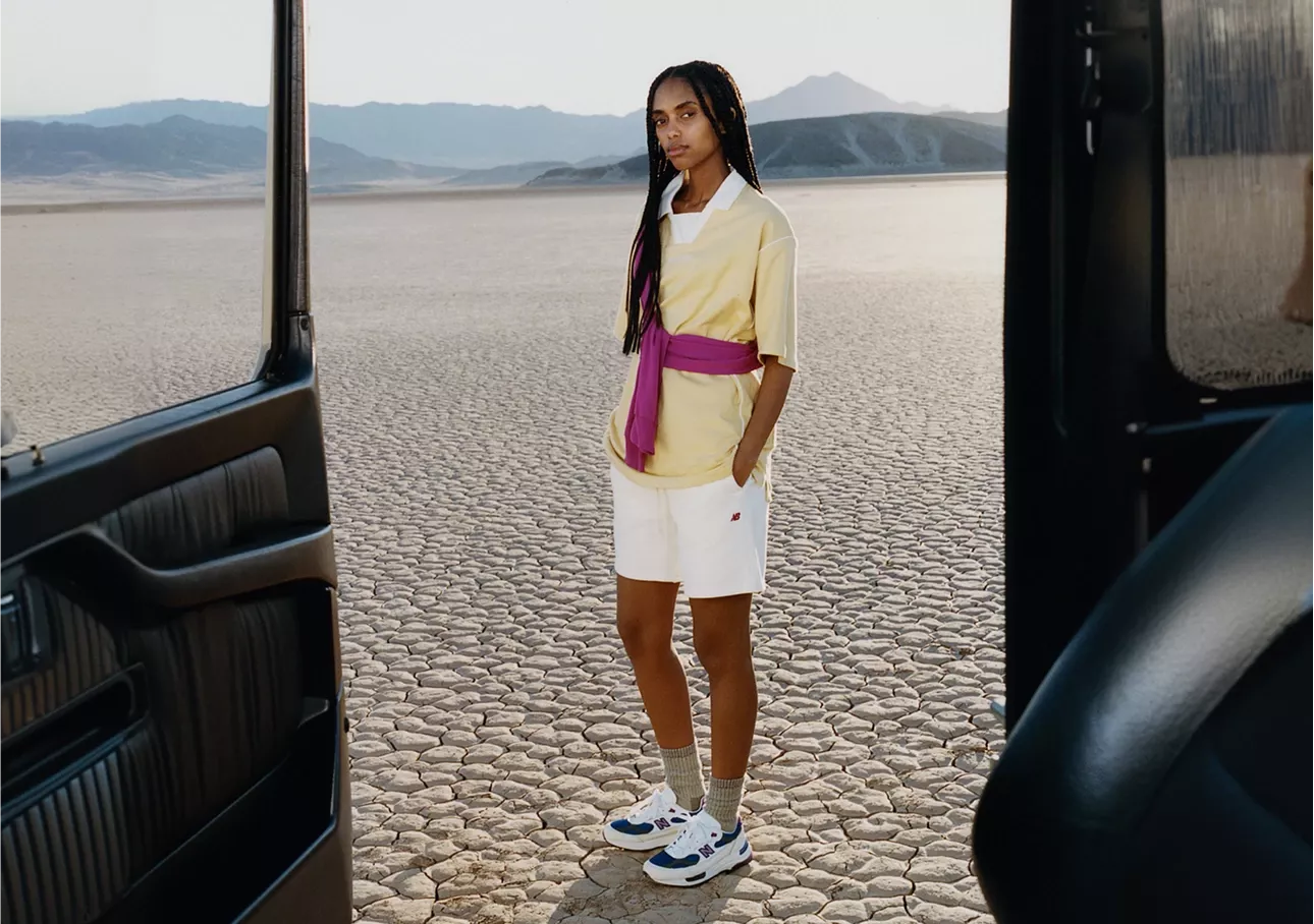 Mulher de polo amarela com suéter rosa nos ombros e tênis Made in USA azul-marinho no deserto